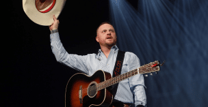 Cody Johnson on stage lifting his hat in the air in Arizona