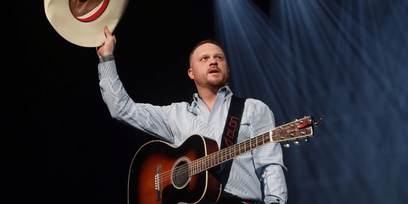 Cody Johnson on stage lifting his hat in the air in Arizona