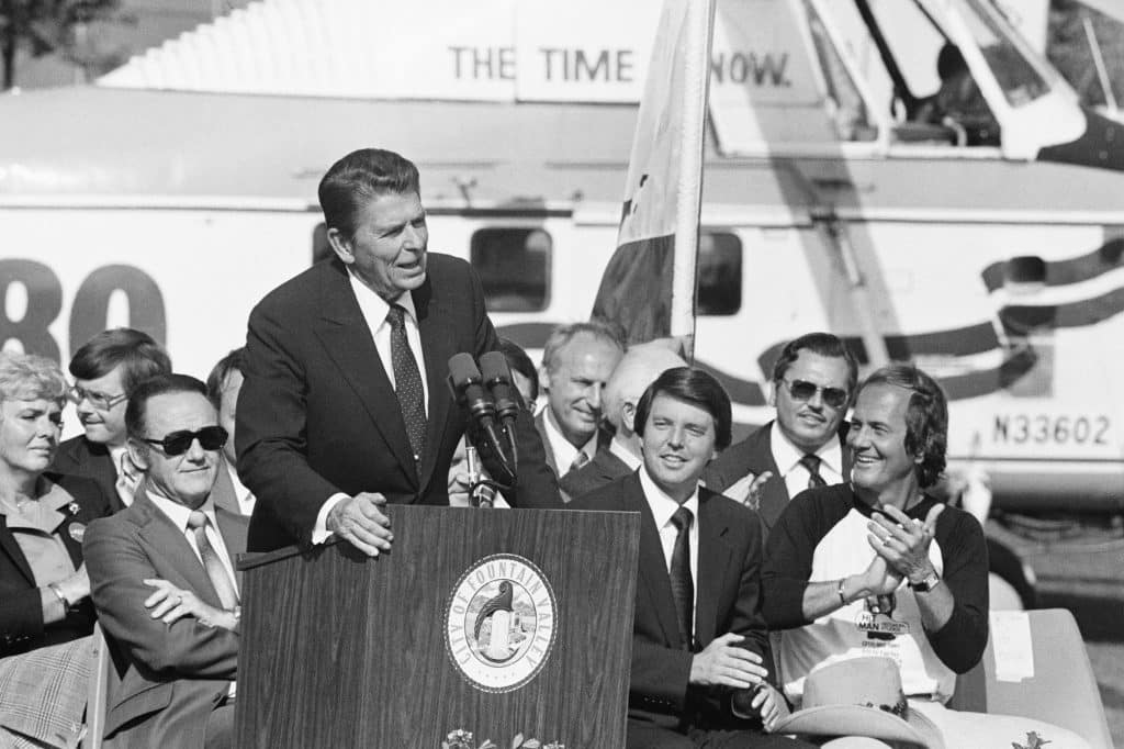 Ronald Reagan is applauded by California Lt. Governor Mike Curb (C) and entertainer pat Boone (R). behind Reagan is one of the helicopters the Reagan party used to campaign in the Southern California Suburbs 10/13.